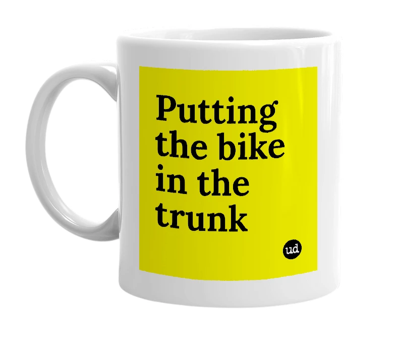 White mug with 'Putting the bike in the trunk' in bold black letters