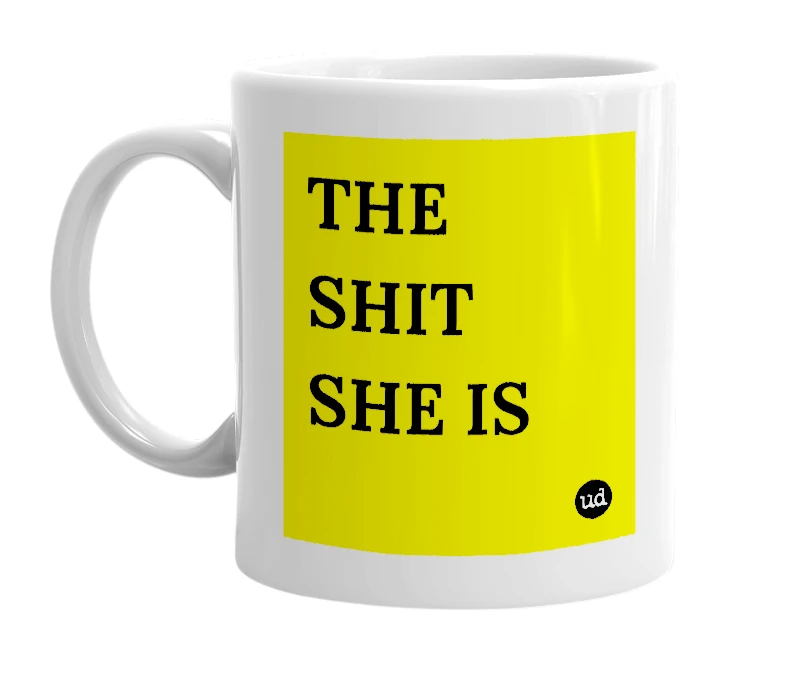 White mug with 'THE SHIT SHE IS' in bold black letters